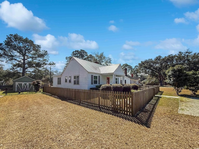 exterior space featuring a fenced front yard, metal roof, an outbuilding, and a yard