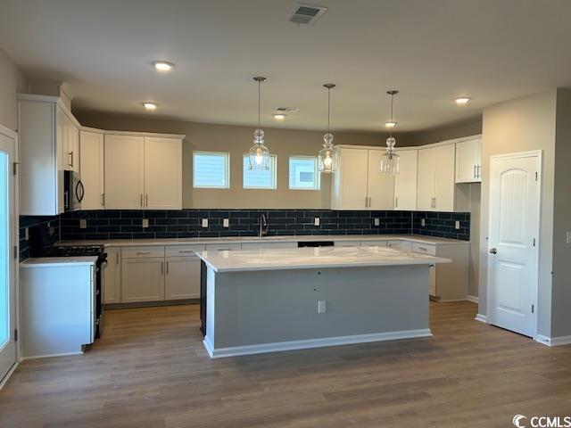 kitchen with black microwave, visible vents, a kitchen island, and white cabinets