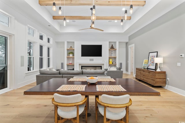 dining room featuring light wood finished floors, baseboards, built in shelves, a fireplace, and beam ceiling