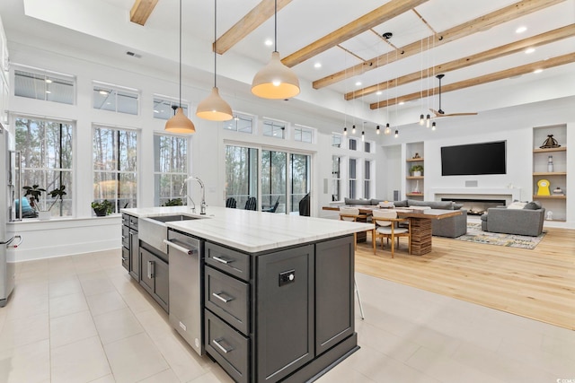 kitchen featuring a kitchen island with sink, a fireplace, built in features, beamed ceiling, and decorative light fixtures