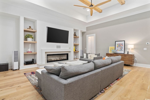 living area featuring baseboards, ceiling fan, wood finished floors, built in shelves, and a fireplace