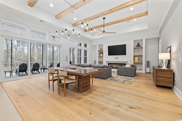 dining room featuring built in features, a glass covered fireplace, wood finished floors, and beamed ceiling