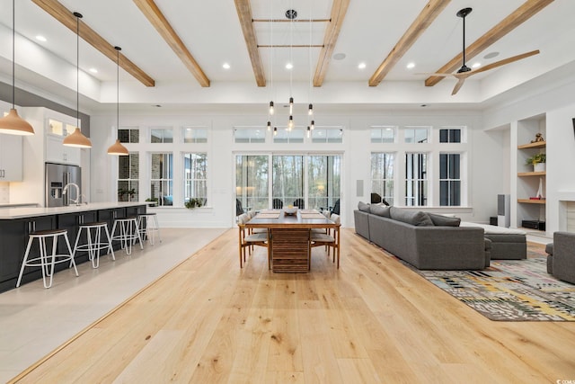 dining space featuring a towering ceiling, light wood-style floors, built in shelves, and beam ceiling