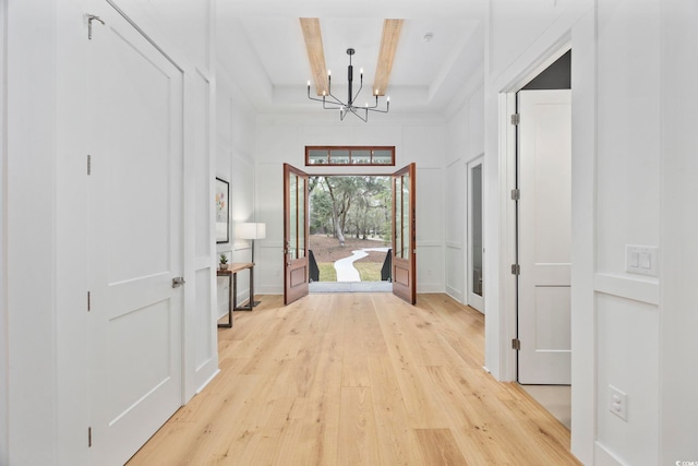 hallway with a decorative wall, coffered ceiling, beam ceiling, light wood finished floors, and an inviting chandelier