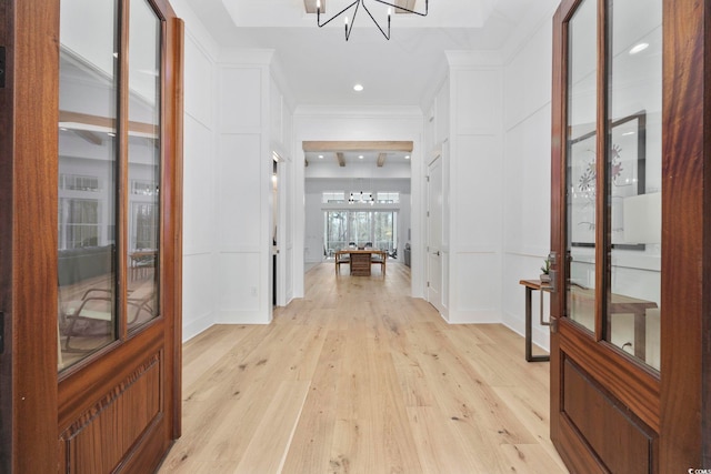 corridor with a notable chandelier, ornamental molding, and light wood-style floors