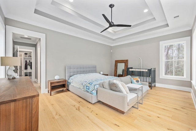 bedroom with a tray ceiling, crown molding, visible vents, light wood-type flooring, and baseboards