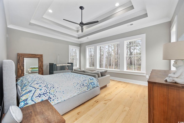 bedroom featuring light wood-type flooring, visible vents, a tray ceiling, and crown molding