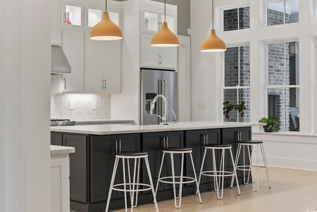 kitchen featuring high end refrigerator, a breakfast bar, light countertops, under cabinet range hood, and white cabinetry