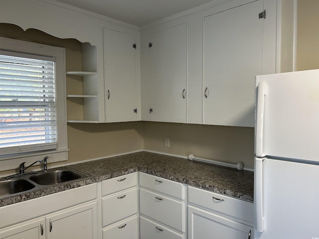 kitchen featuring dark countertops, white cabinetry, freestanding refrigerator, and a sink