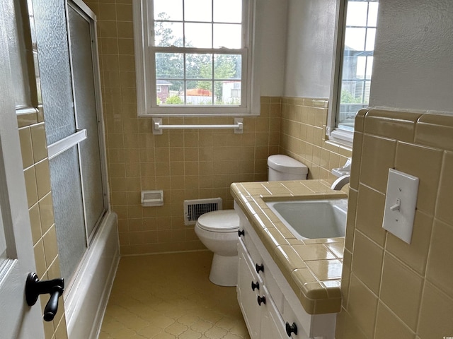 full bathroom with enclosed tub / shower combo, toilet, vanity, visible vents, and tile walls