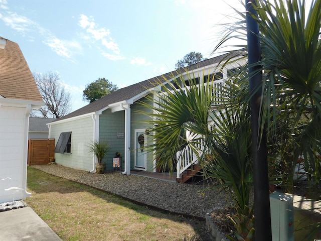 view of side of property with a shingled roof and fence