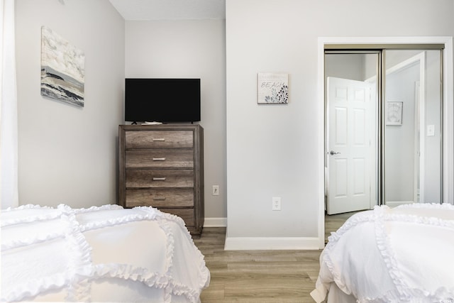 bedroom with a closet, light wood-style flooring, and baseboards