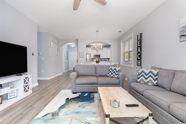 living area with light wood-type flooring, baseboards, arched walkways, and ceiling fan with notable chandelier