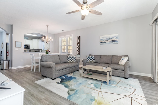 living area with arched walkways, baseboards, light wood finished floors, and ceiling fan with notable chandelier