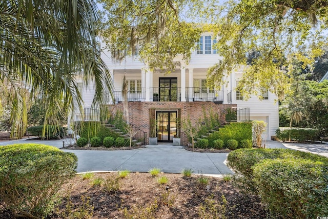 entrance to property with a garage, brick siding, a porch, and french doors