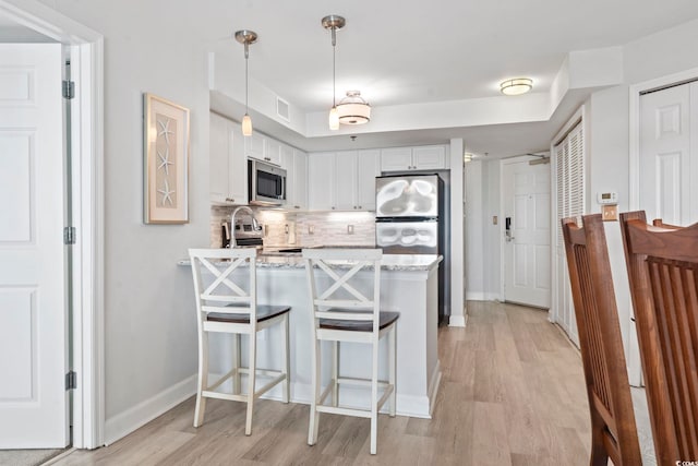 kitchen with light wood finished floors, backsplash, appliances with stainless steel finishes, white cabinetry, and a peninsula