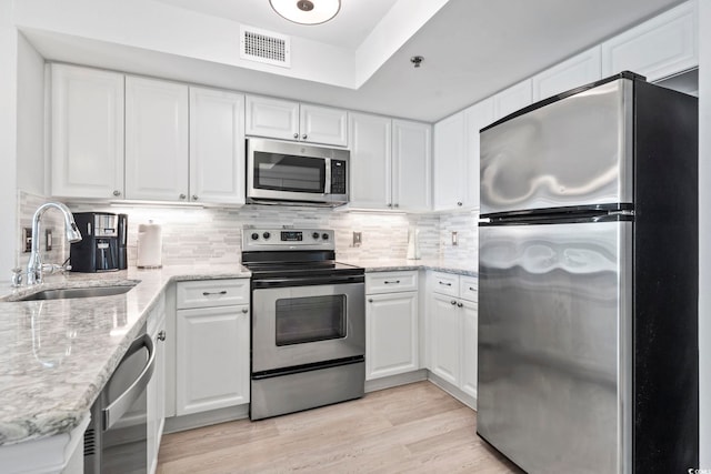 kitchen featuring light wood-style flooring, stainless steel appliances, a sink, visible vents, and white cabinetry