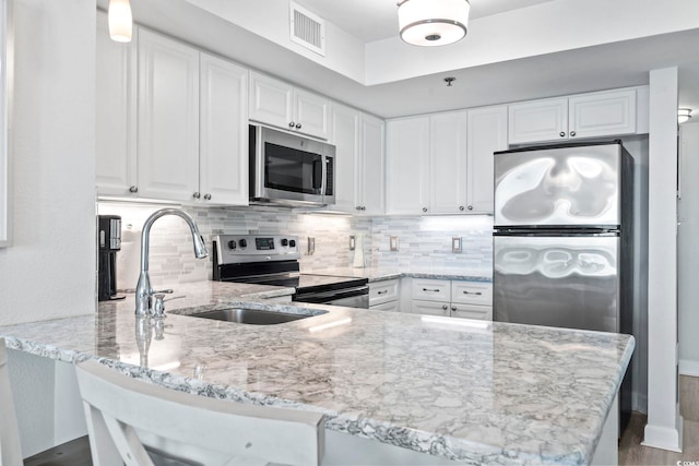 kitchen with visible vents, light stone counters, a peninsula, stainless steel appliances, and backsplash