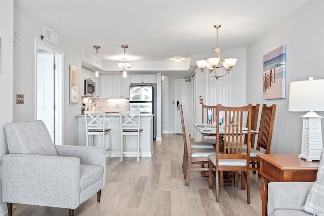 dining area with light wood-style floors, visible vents, and a notable chandelier