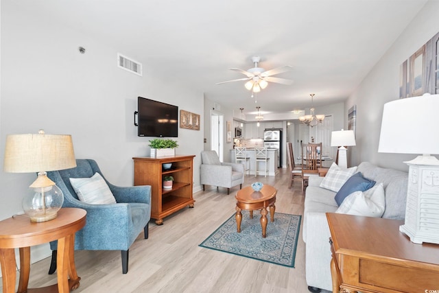 living room featuring ceiling fan with notable chandelier, light wood-style flooring, and visible vents