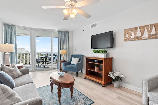 living room with light wood-type flooring, baseboards, visible vents, and ceiling fan