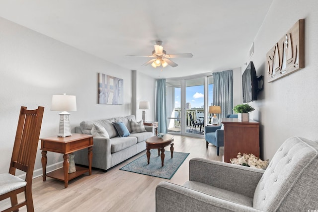 living room featuring a ceiling fan, expansive windows, baseboards, and light wood finished floors