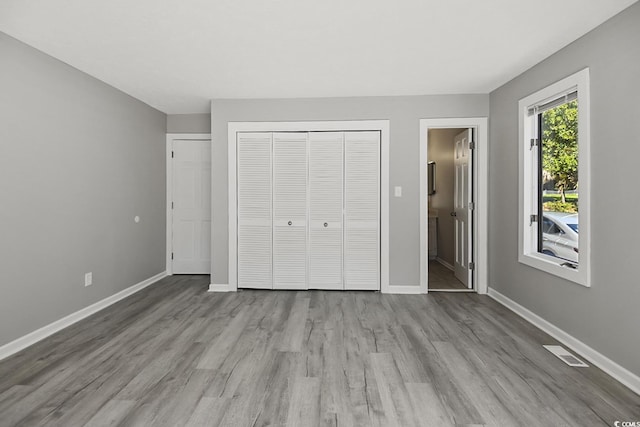 unfurnished bedroom with baseboards, visible vents, wood finished floors, ensuite bathroom, and a closet