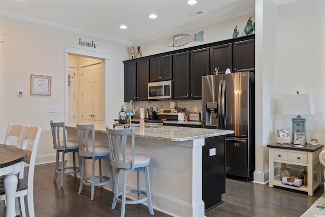 kitchen with dark wood-style flooring, crown molding, a center island with sink, tasteful backsplash, and appliances with stainless steel finishes