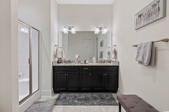 bathroom featuring double vanity, a stall shower, a sink, and baseboards