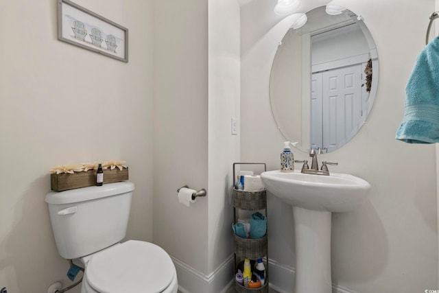 half bath with toilet, baseboards, and a sink