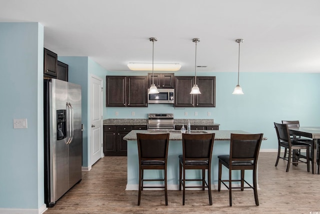 kitchen featuring stainless steel appliances, light wood-type flooring, dark brown cabinetry, and a kitchen breakfast bar