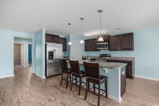 kitchen featuring visible vents, appliances with stainless steel finishes, dark brown cabinets, light wood-style floors, and a kitchen bar