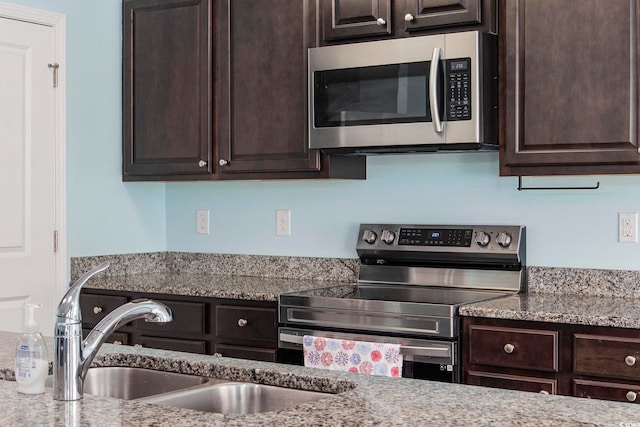 kitchen featuring stainless steel appliances, dark brown cabinets, a sink, and light stone counters