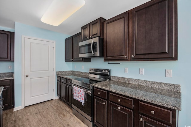 kitchen featuring dark stone counters, stainless steel appliances, dark brown cabinetry, and light wood-style floors