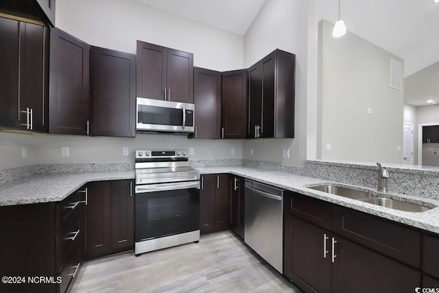 kitchen with light wood finished floors, appliances with stainless steel finishes, light stone counters, dark brown cabinets, and a sink