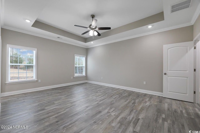 spare room featuring crown molding, a raised ceiling, visible vents, wood finished floors, and baseboards