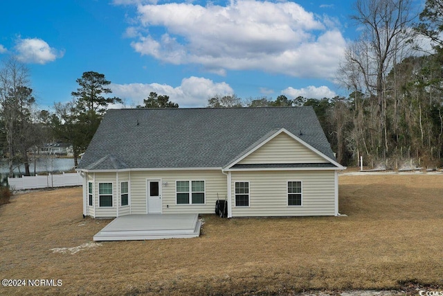 rear view of property featuring roof with shingles, a deck, and a yard