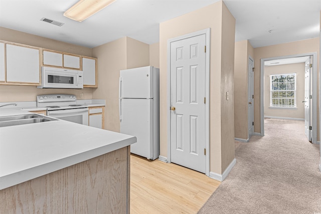 kitchen featuring light countertops, visible vents, light wood finished floors, white appliances, and a sink