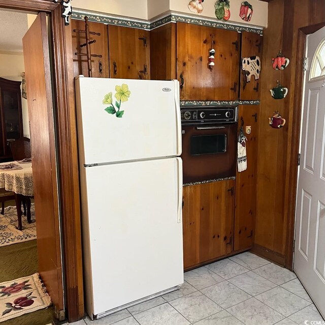 kitchen with wood walls, wall oven, freestanding refrigerator, and brown cabinets