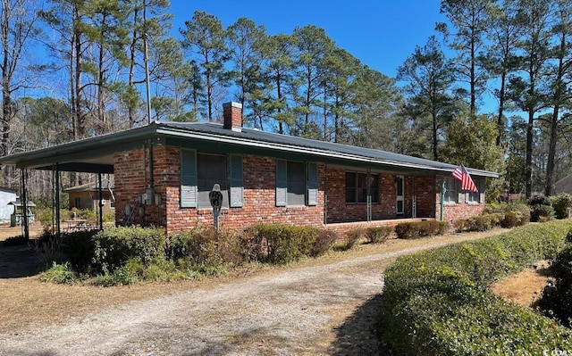 view of home's exterior featuring driveway, a chimney, an attached carport, and brick siding