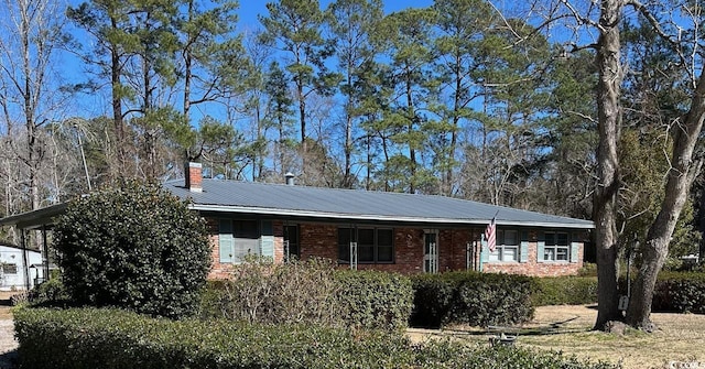 ranch-style house with a chimney, metal roof, and brick siding