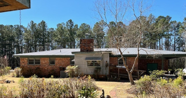 rear view of property featuring a chimney, metal roof, and brick siding