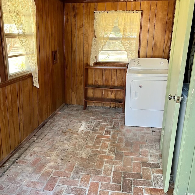 clothes washing area featuring laundry area, wood walls, brick floor, and washer / dryer