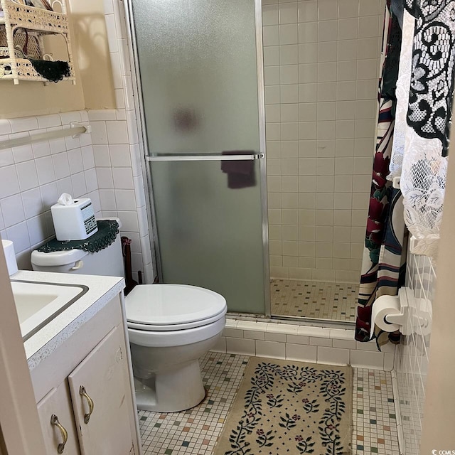 bathroom with toilet, vanity, tile walls, a shower stall, and tile patterned floors