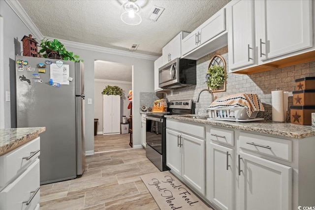 kitchen with stainless steel appliances, white cabinets, ornamental molding, and decorative backsplash