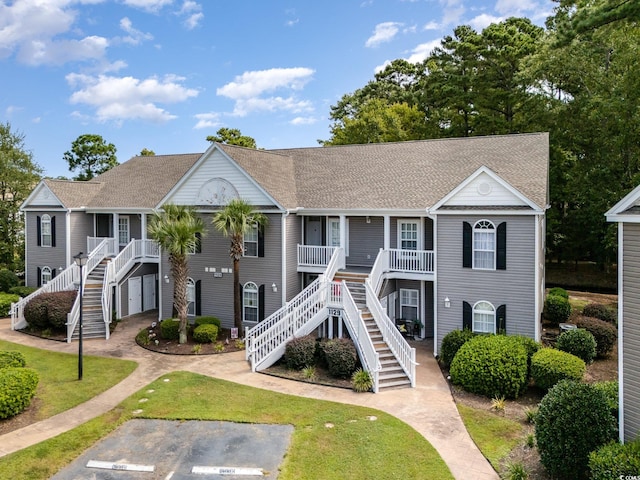 coastal home with roof with shingles, a porch, stairway, and a front yard