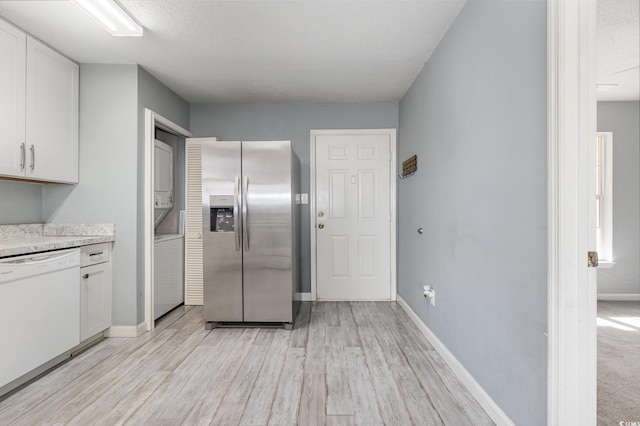 kitchen with white dishwasher, stacked washer / dryer, baseboards, white cabinets, and stainless steel refrigerator with ice dispenser