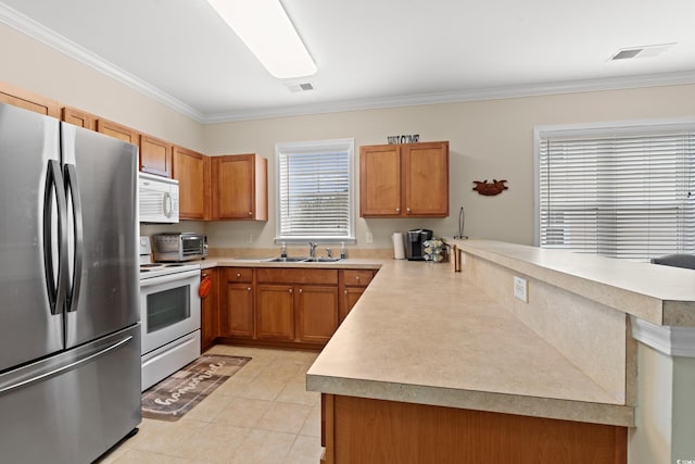 kitchen with ornamental molding, brown cabinetry, a sink, white appliances, and a peninsula