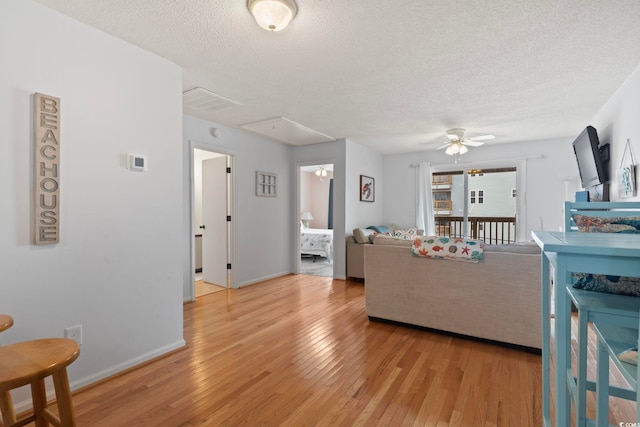 living area with light wood finished floors, attic access, baseboards, ceiling fan, and a textured ceiling