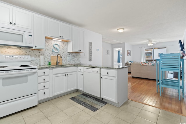 kitchen featuring white appliances, light tile patterned floors, white cabinets, a peninsula, and a sink